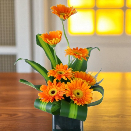Featuring 7 bold and beautiful orange gerberas, this arrangement is artistically styled with fresh Victoria leaves that enhance its natural charm. - YHOJA.COM