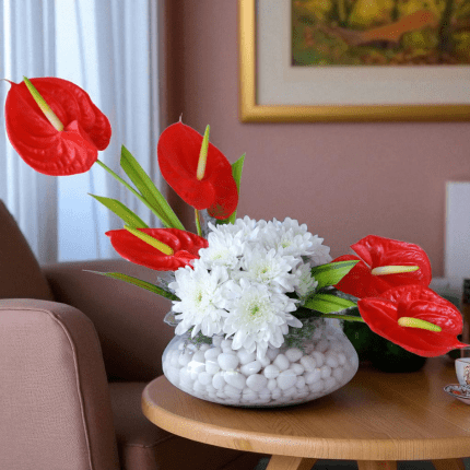 Red anthurium and white daisy vase arrangement with decorative stones